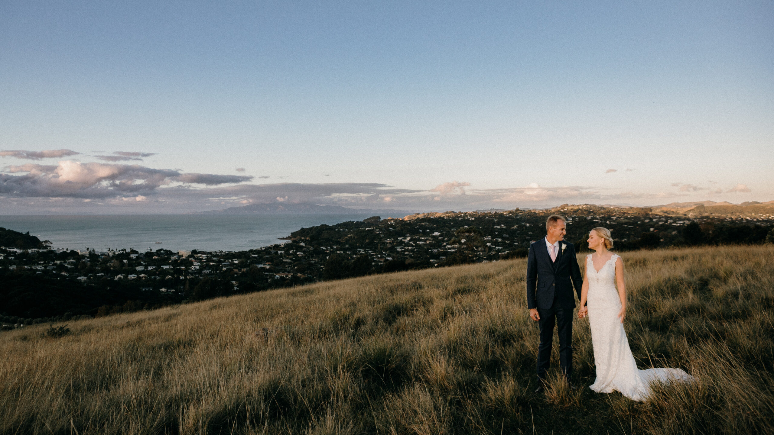 Bride and Groom wedding photos ontop hill in long grass with view of ocean at Mudbrick Waiheke Island Auckland, photo by Sarah Weber Photography