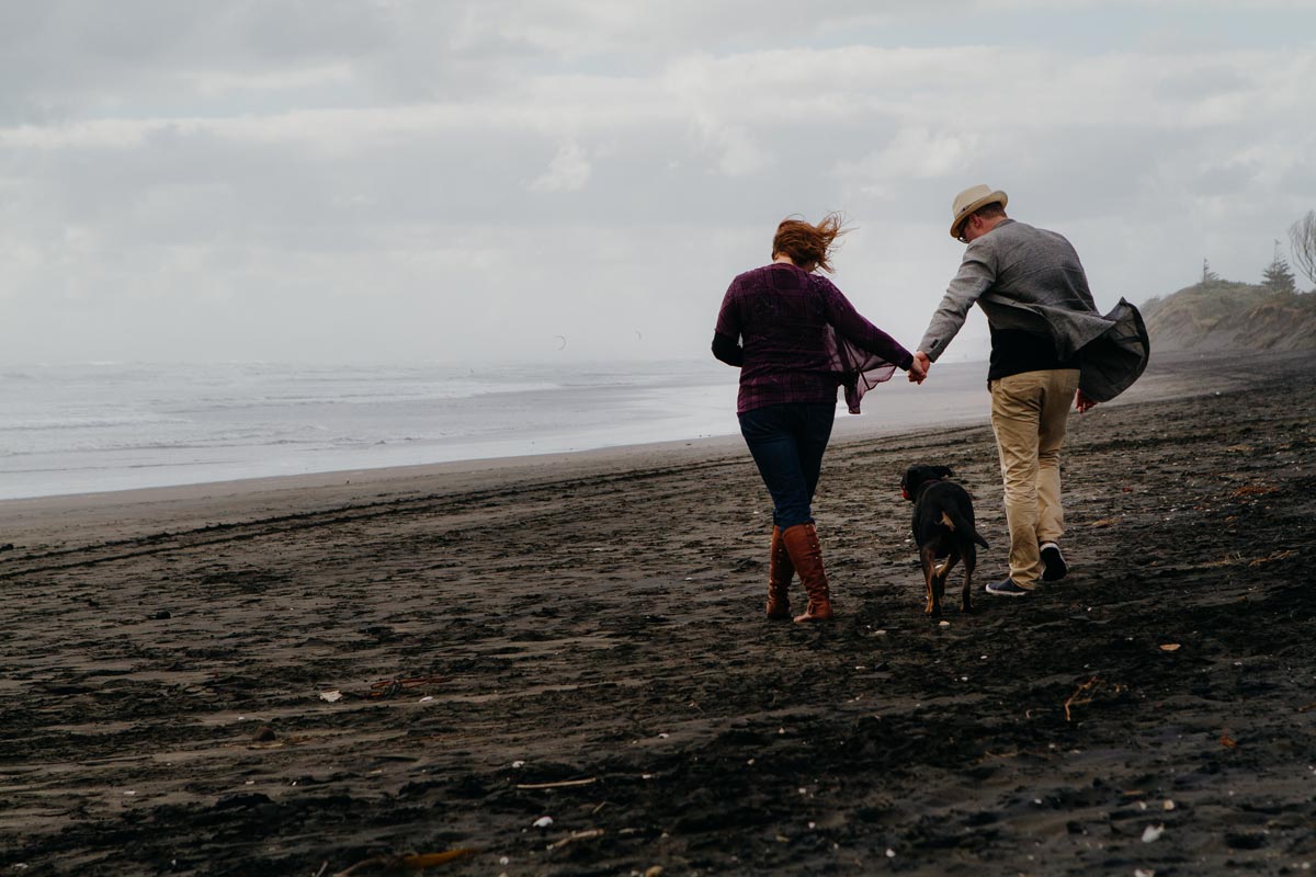 Pet portrait photo of dog and owners walking on muriwai beach in auckland by sarah weber photography
