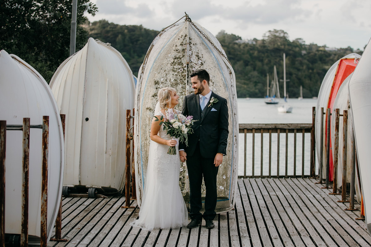 Bride and Groom posing infront of dinghy at Herald Island Wharf in Whenuapai, Auckland photo by Sarah Weber Photography