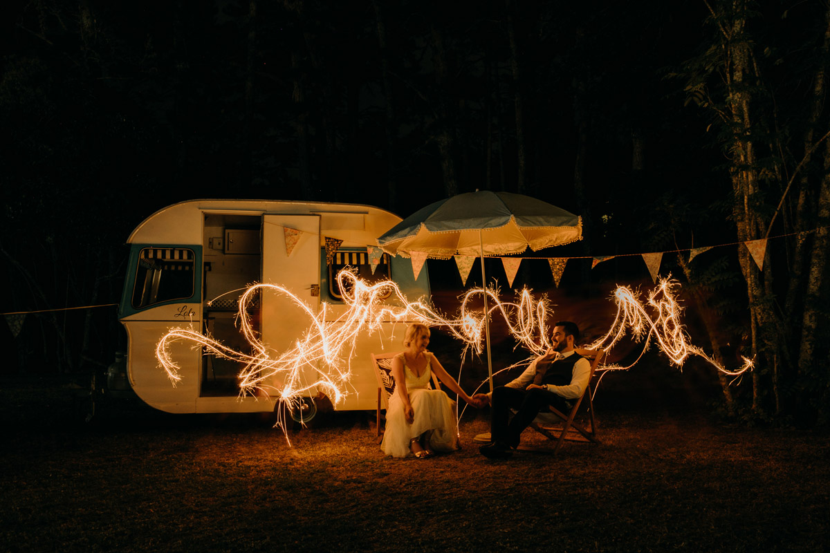 Bride and Groom sit infront of caravan with long exposure sparklers at The Brigham wedding reception photo by Sarah Weber Photography