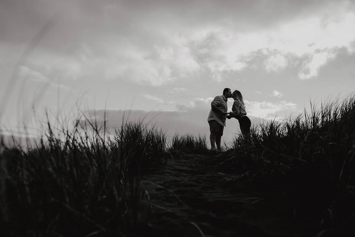 silhouette of couple kissing at muriwai beach auckland new zealand during a golden light evening lifestyle engagment pre-wedding photoshoot session by sarah weber photography