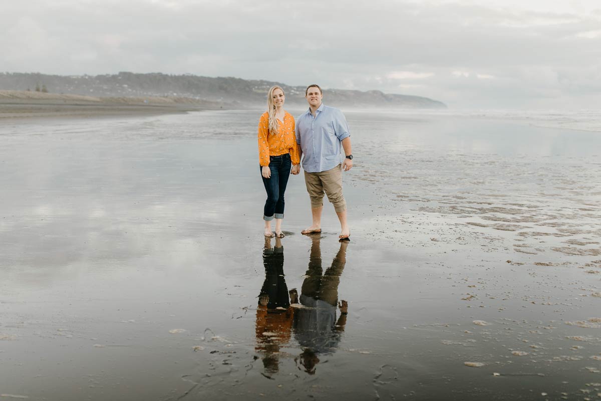 couple portrait reflection muriwai beach auckland new zealand during a golden light evening lifestyle engagment pre-wedding photoshoot session by sarah weber photography